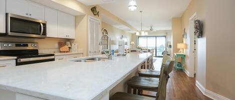 A modern kitchen with white cabinets, a large island, stainless steel appliances, and pendant lighting.