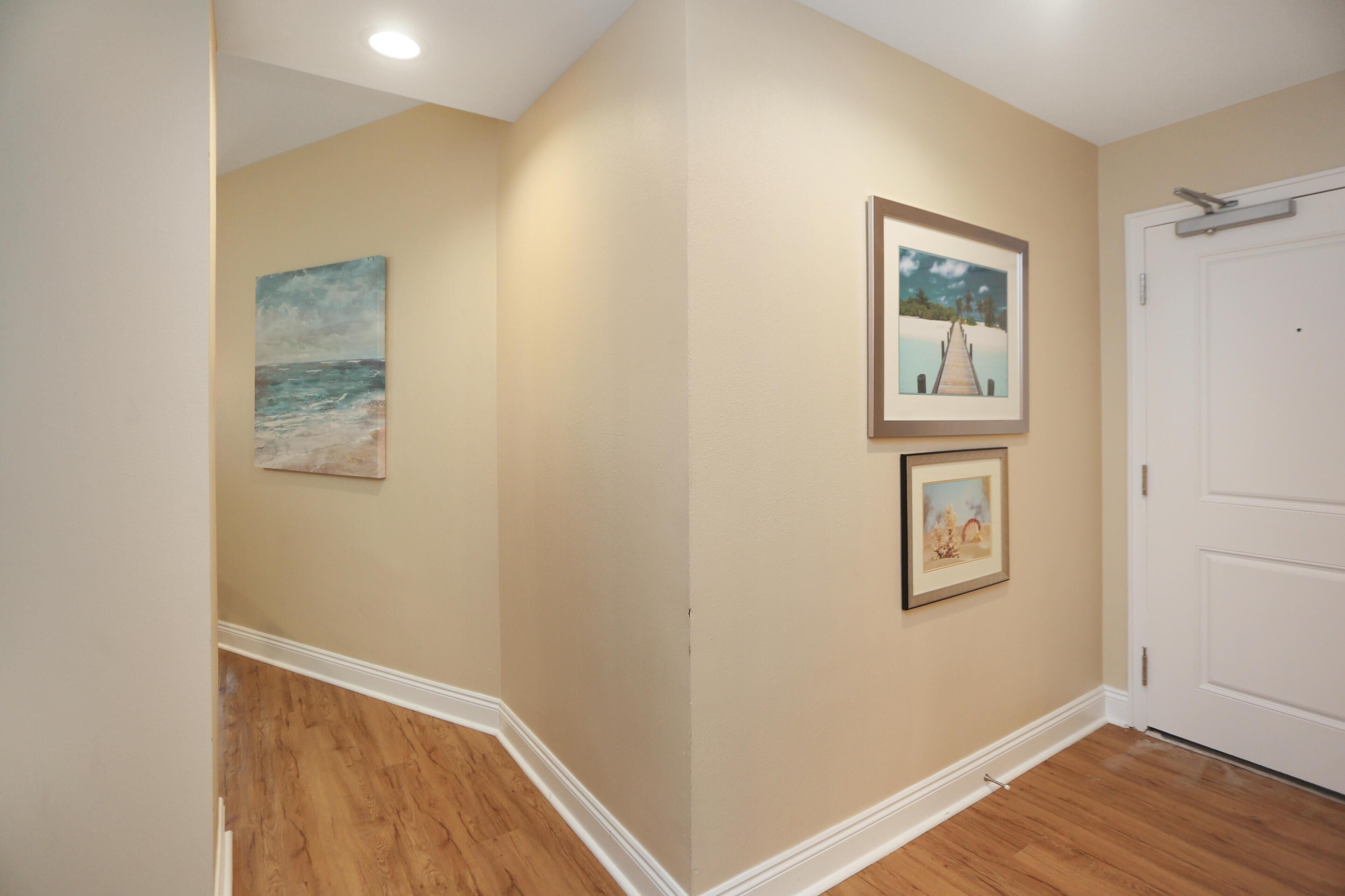 A hallway with wooden flooring, beige walls, and three framed pictures.