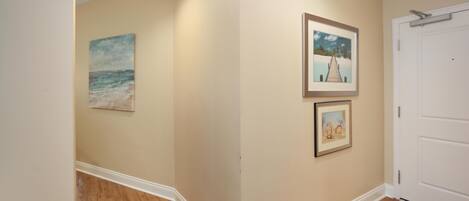 A hallway with wooden flooring, beige walls, and three framed pictures.