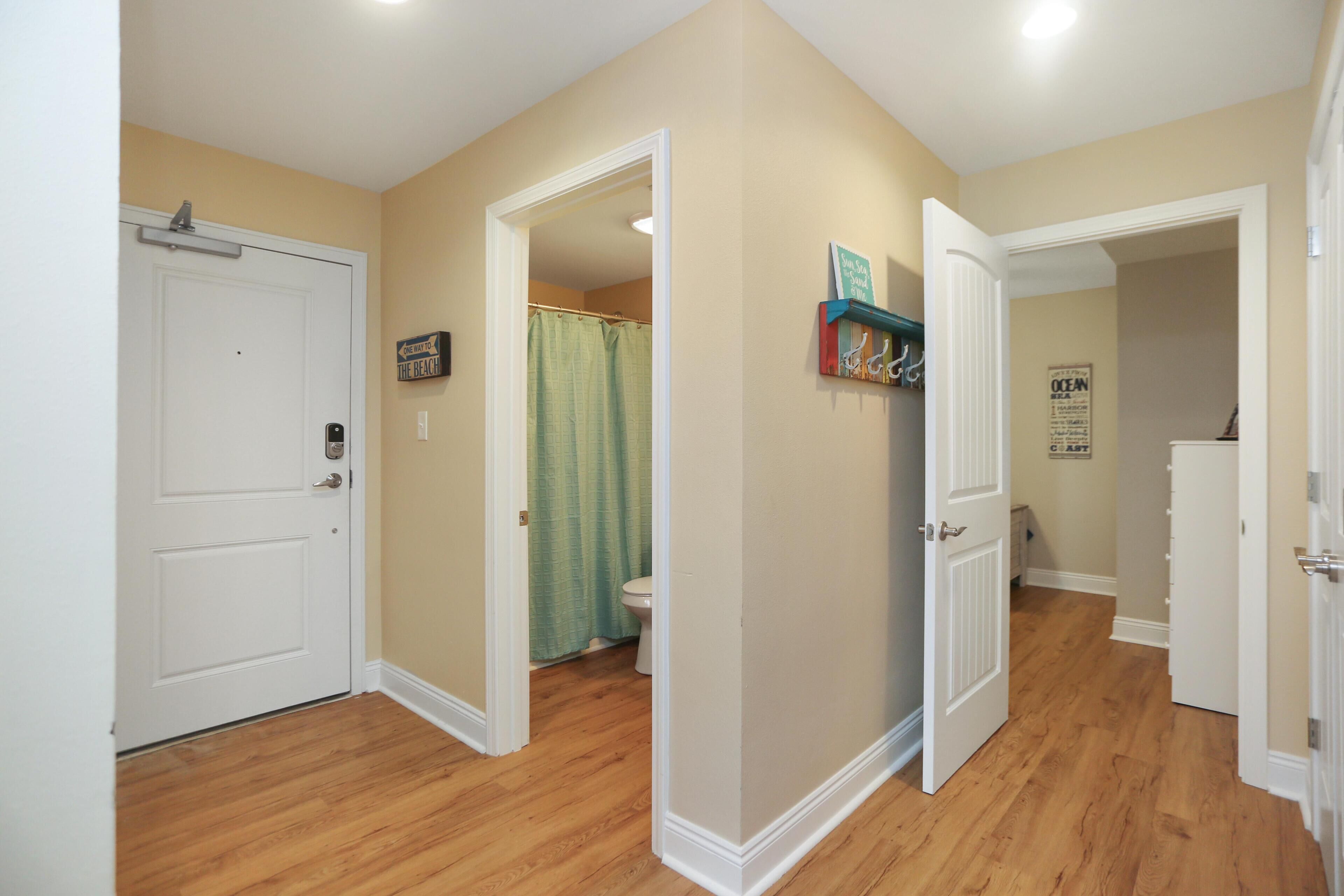 A hallway with wooden flooring, white doors, and a bathroom with a shower curtain.