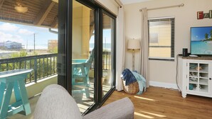 A balcony with a table and chairs, a sliding glass door, a TV on a cabinet, and a view of the beach. - Club at Mexico Beach 2D (Port St. Joe)