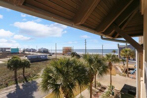 A view from a balcony overlooking a beach with palm trees, a road, and buildings in the distance. - Club at Mexico Beach 2D (Port St. Joe)