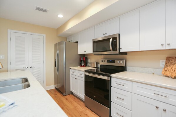A modern kitchen with white cabinets, stainless steel appliances, and a wooden floor. - Club at Mexico Beach 2D (Port St. Joe)