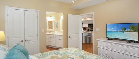 A bedroom with a bed, a dresser, and a television displaying a beach scene.