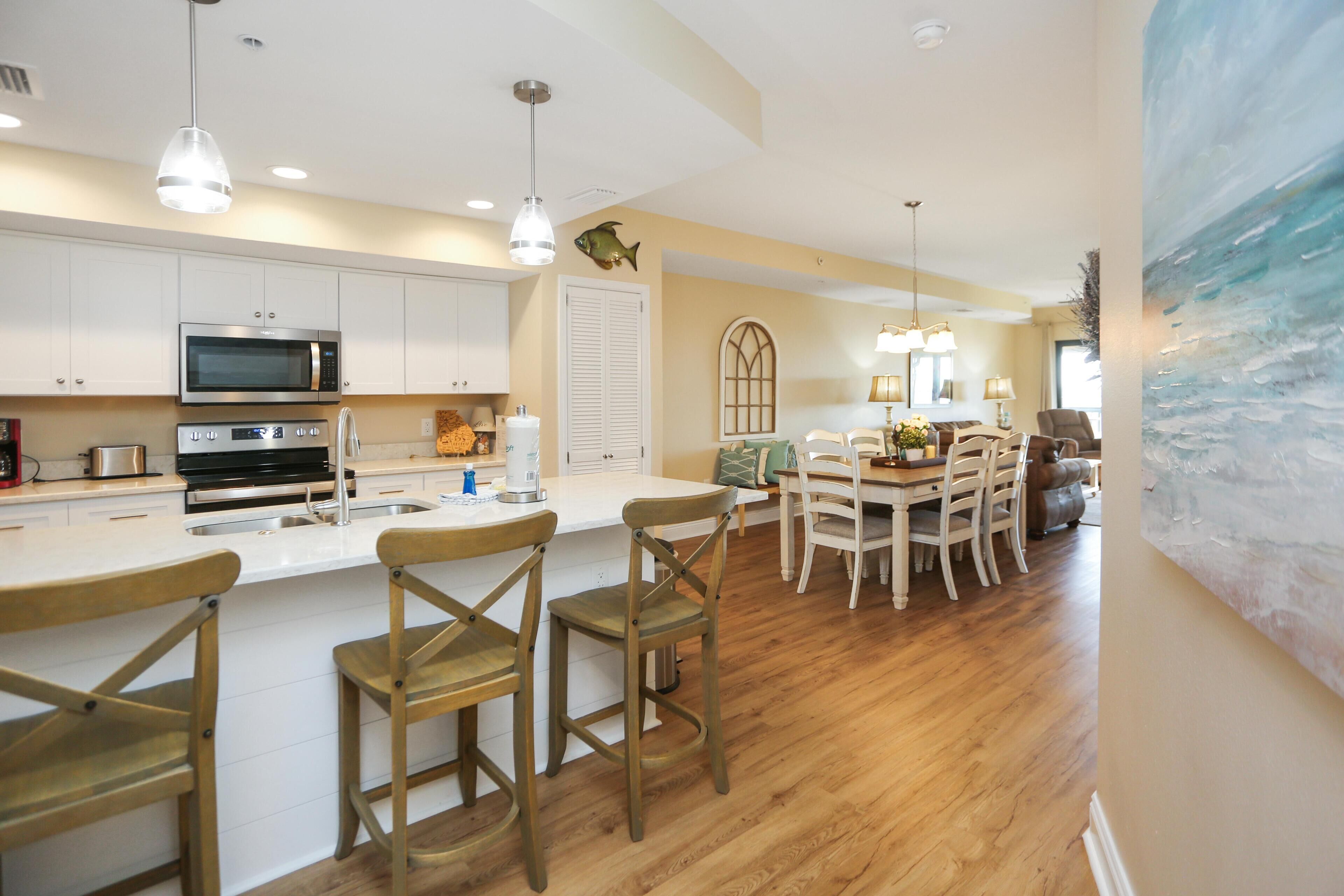 A modern kitchen with white cabinets, a large island with bar stools, and a dining area with a wooden table and chairs.