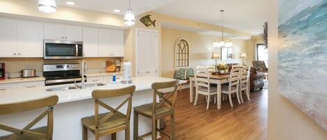 A modern kitchen with white cabinets, a large island with bar stools, and a dining area with a wooden table and chairs.