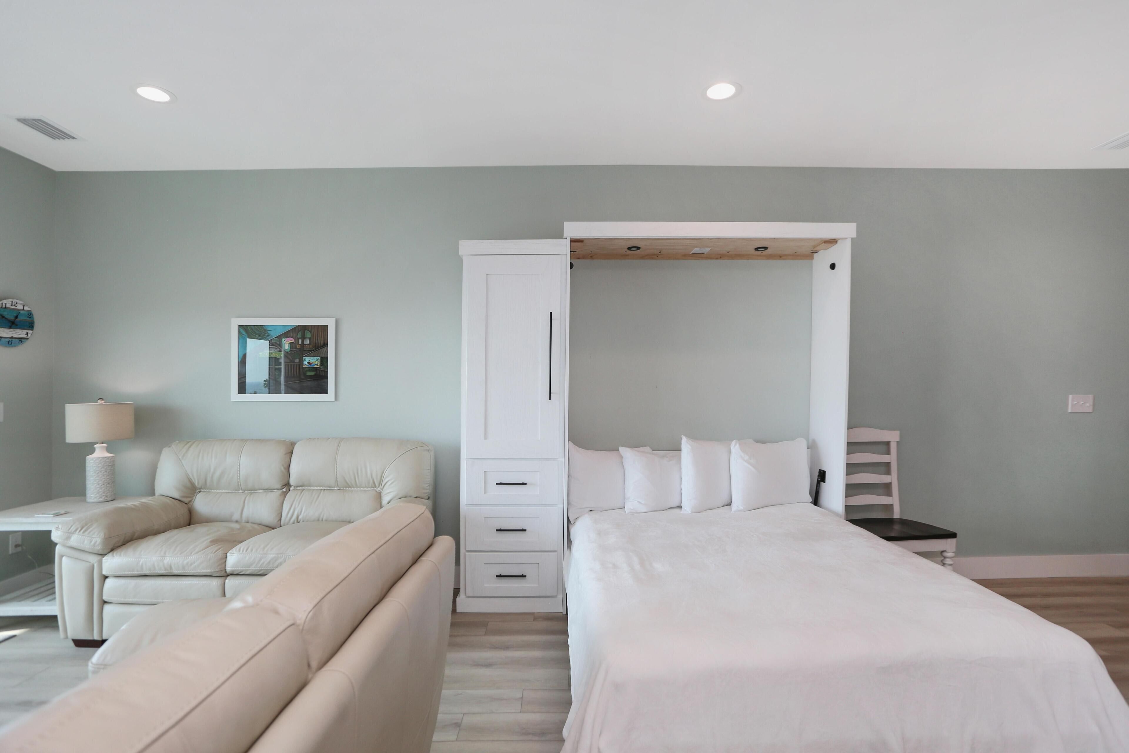 A modern bedroom with a large bed, a sofa, a desk, and a wardrobe.
