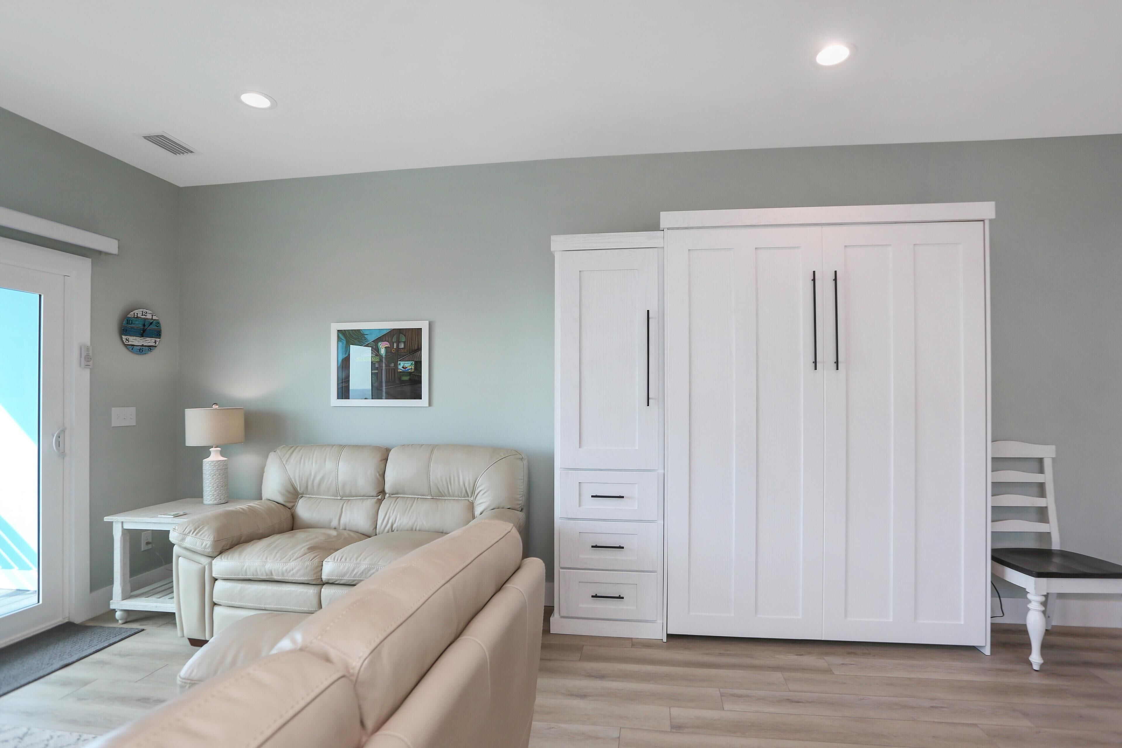 Een moderne woonkamer met een beige bank, een witte garderobe en een kleine tafel met een lamp.