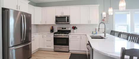 Una cocina moderna con armarios blancos, electrodomésticos de acero inoxidable, una isla grande e iluminación colgante.