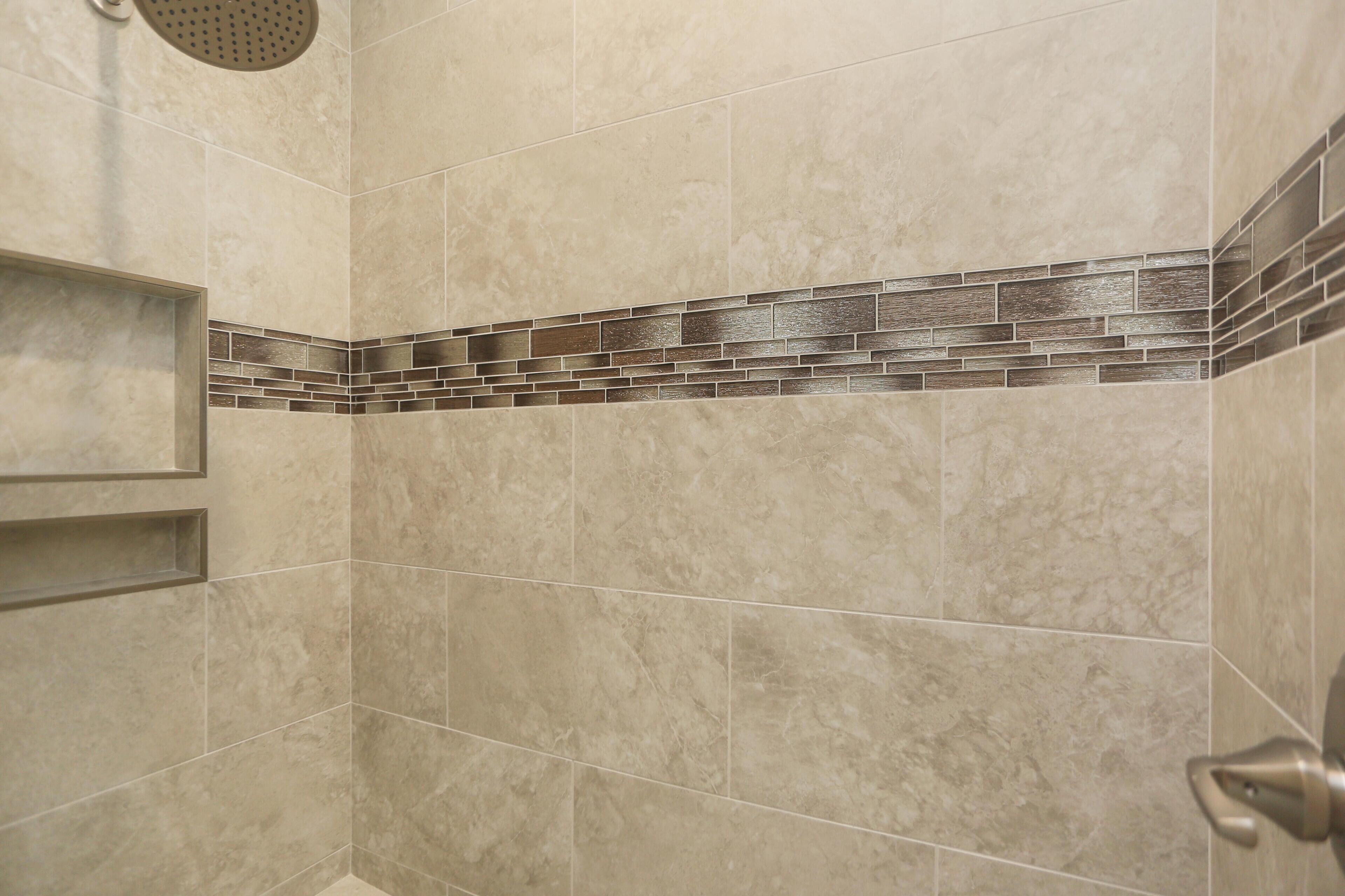 A shower area with beige tiles and a decorative brick pattern along the lower wall.