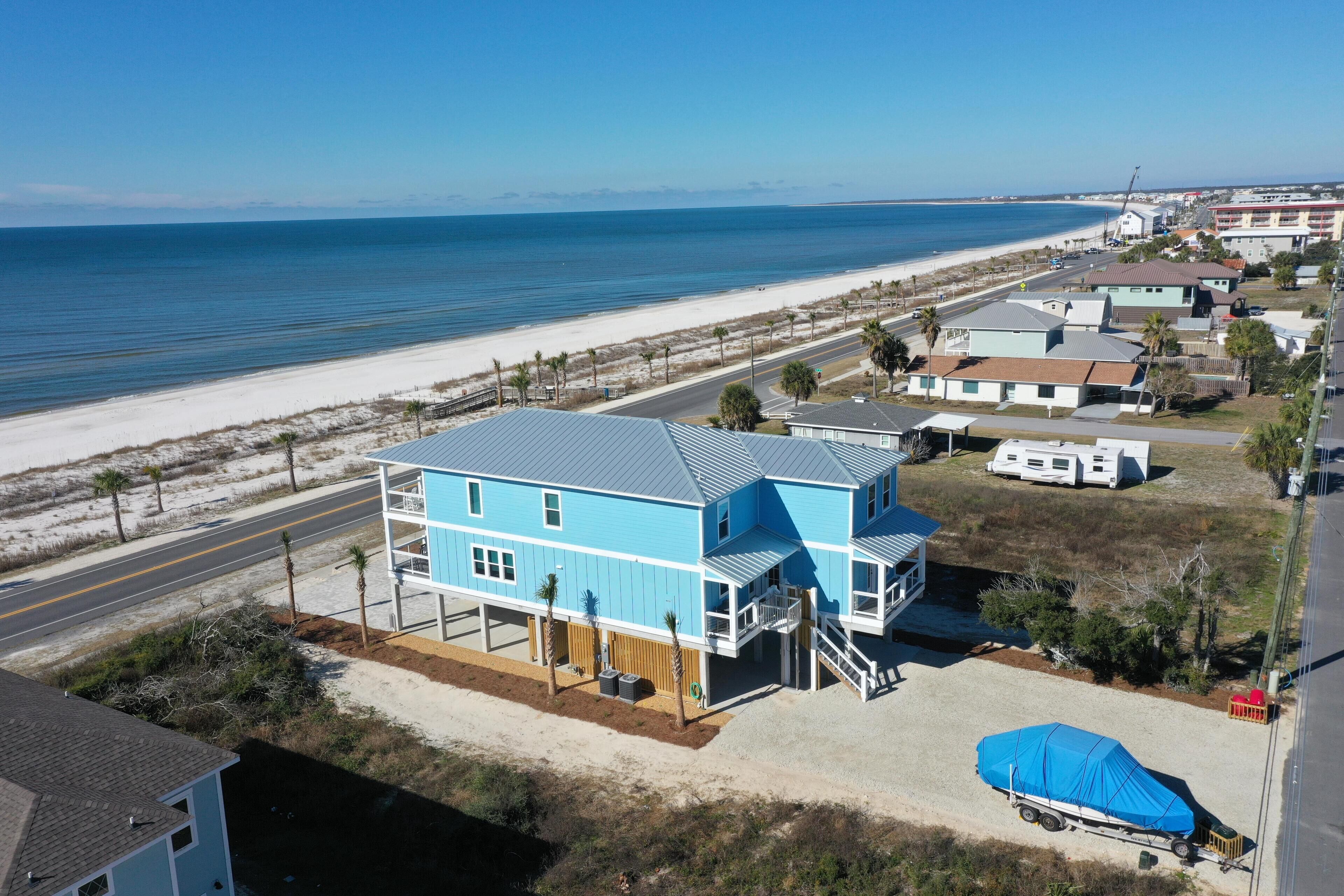 A coastal property with a large blue house, a beach view, and a trailer on the property.