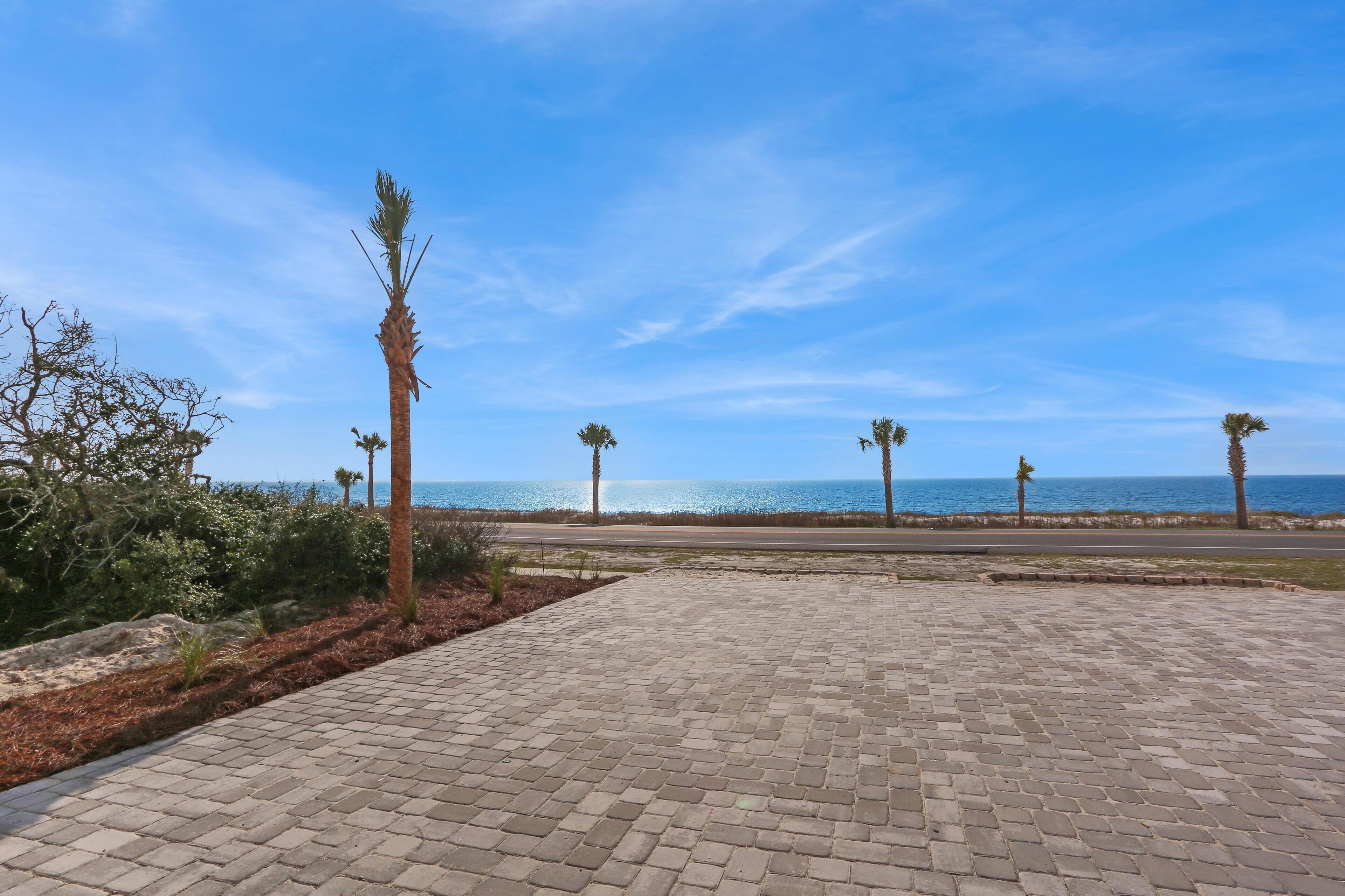 A paved walkway with palm trees and a view of the sea.