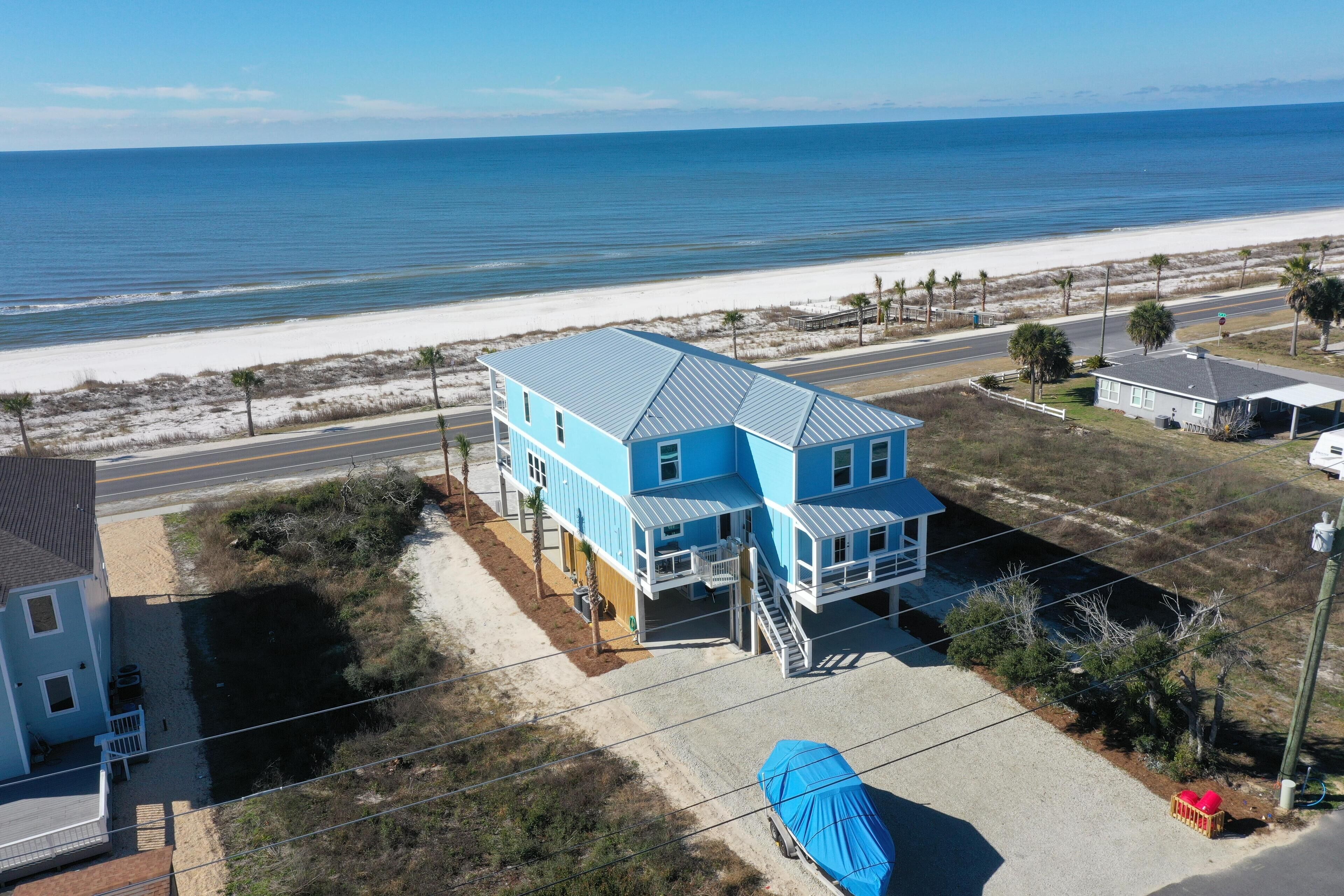 A two-story blue house with a balcony, located near a beach and a road.