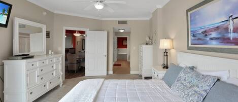 A bedroom with a large bed, a ceiling fan, a dresser, and a painting on the wall.