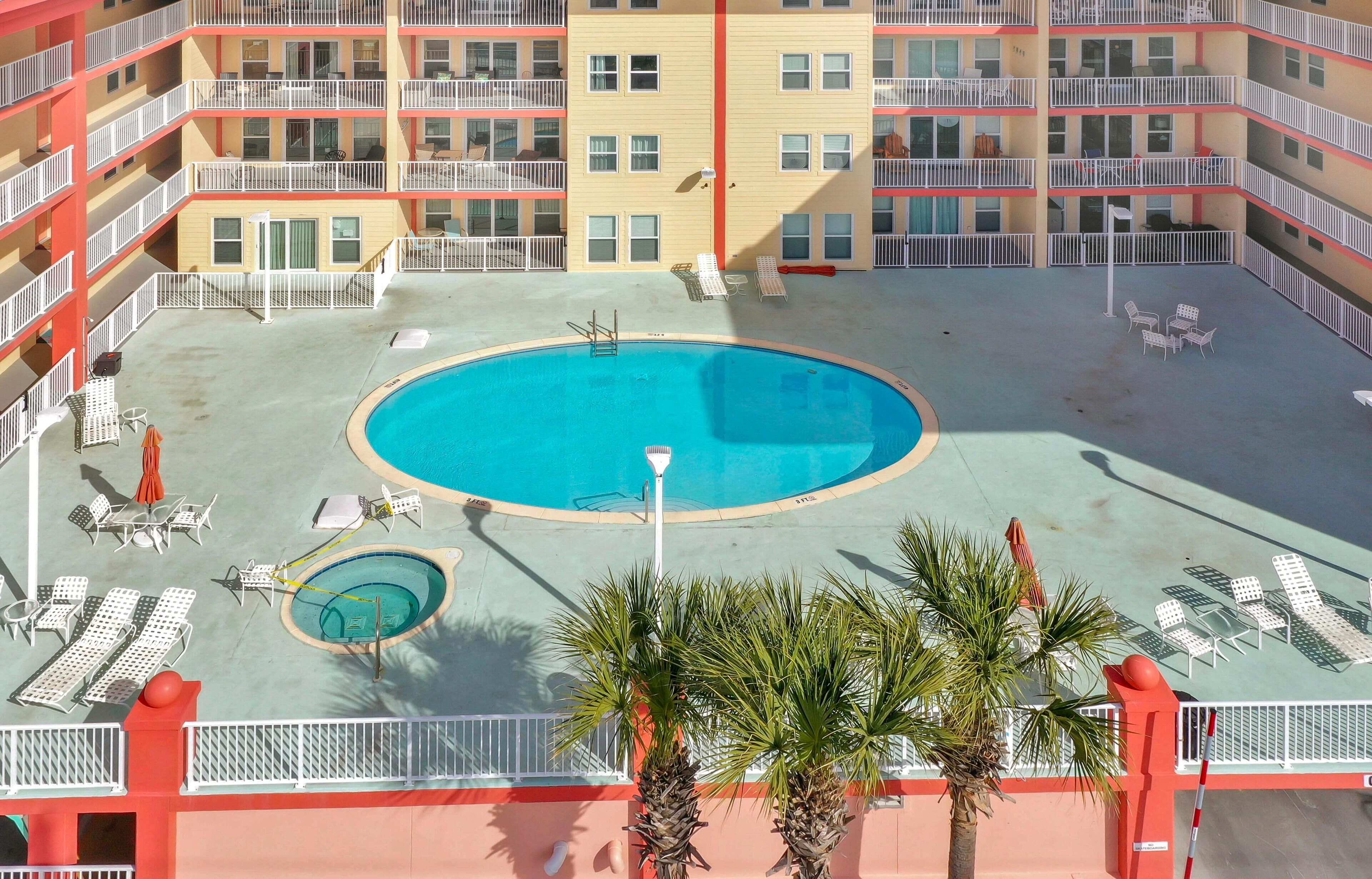 A rooftop pool area with sun loungers, a small pool, and palm trees.
