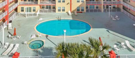 A rooftop pool area with sun loungers, a small pool, and palm trees.