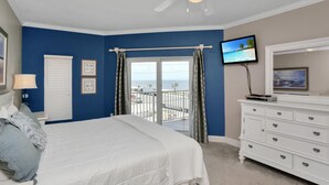 Een slaapkamer met een bed, een dressoir, een televisie en een balkon met uitzicht op de oceaan.