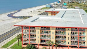 Een hotel met meerdere verdiepingen, balkons, uitzicht op het strand en een parkeerplaats.