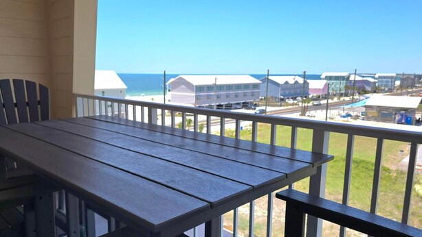 A balcony with a wooden table and chairs, overlooking a beach and buildings. - Paradise Shores 403 Sunset Paradise (Port St. Joe)