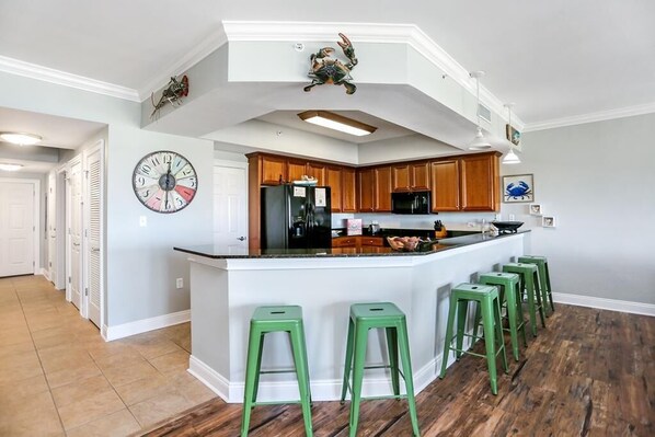 Une cuisine dotée d’un îlot central, de meubles en bois et de tabourets de bar verts.