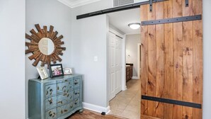 A hallway with a wooden floor, a blue dresser with drawers, a mirror with a sunburst design, and a sliding barn door. - Paradise Shores 403 Sunset Paradise (Port St. Joe)
