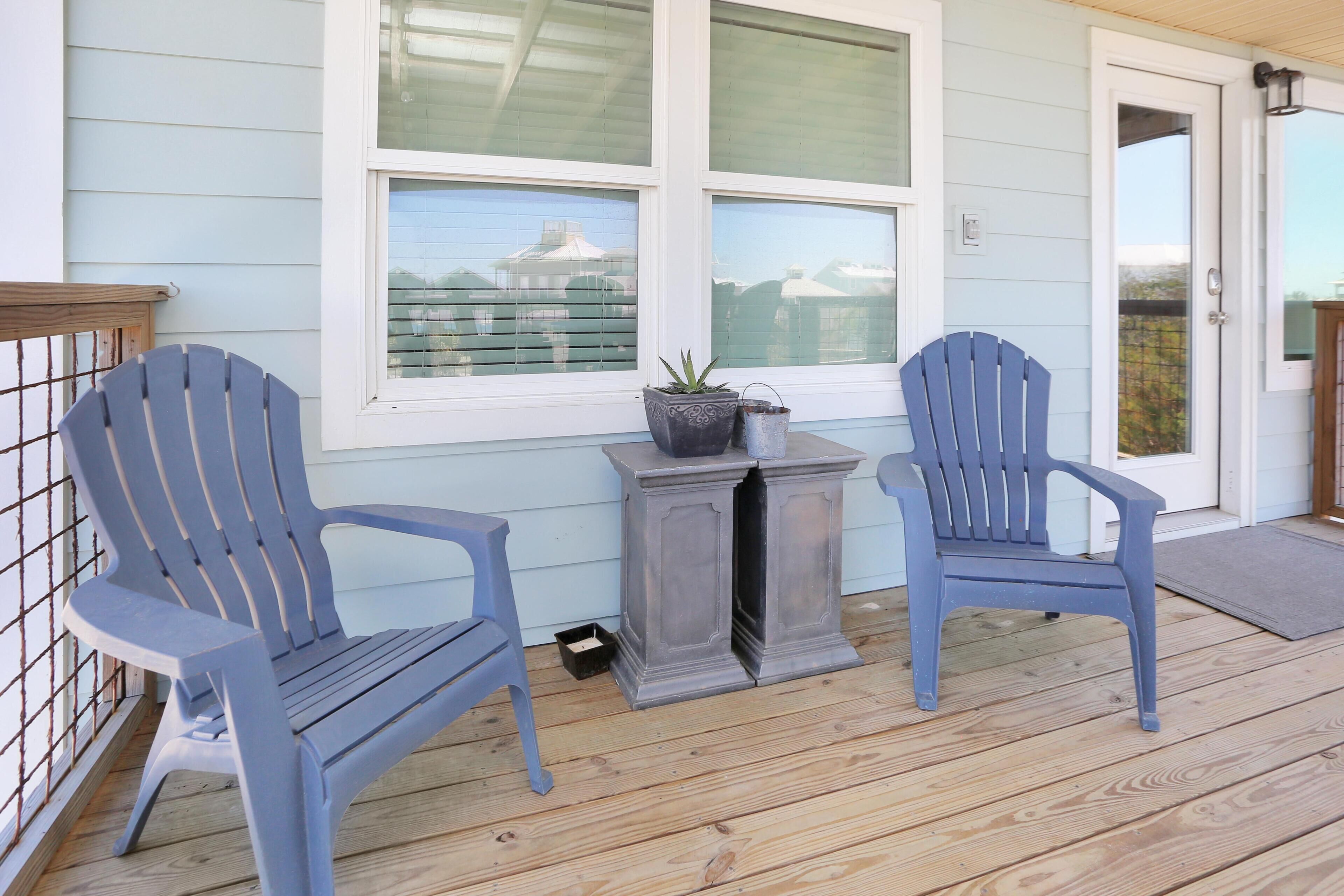 Une véranda avec deux fauteuils Adirondack, une petite table sur laquelle est posée une plante en pot, et une porte avec un panneau de verre.