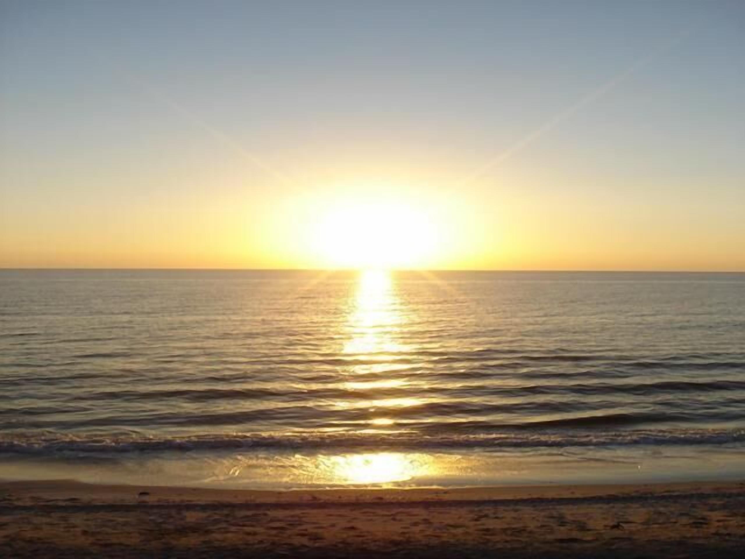 A sunset over a calm sea with a beach in the foreground.