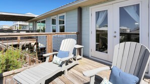 A wooden deck with two Adirondack chairs and a table, a sliding glass door, and a view of a house in the background. - Salt Cured (Port St. Joe)
