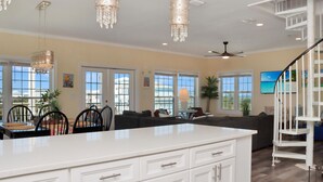 A spacious living area with a white island, dining table, and chairs, a staircase, and large windows. - The Chill Inn (Port St. Joe)