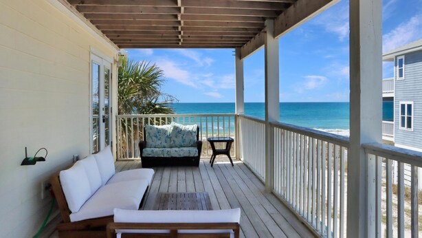 A wooden deck with a sofa and a small table, overlooking a beach and ocean. - The Chill Inn (Port St. Joe)
