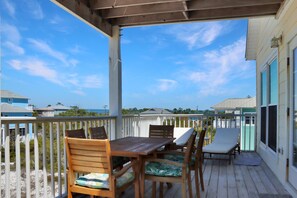 A wooden deck with a table and chairs, a lounge chair, and a view of the ocean and other buildings. - The Chill Inn (Port St. Joe)