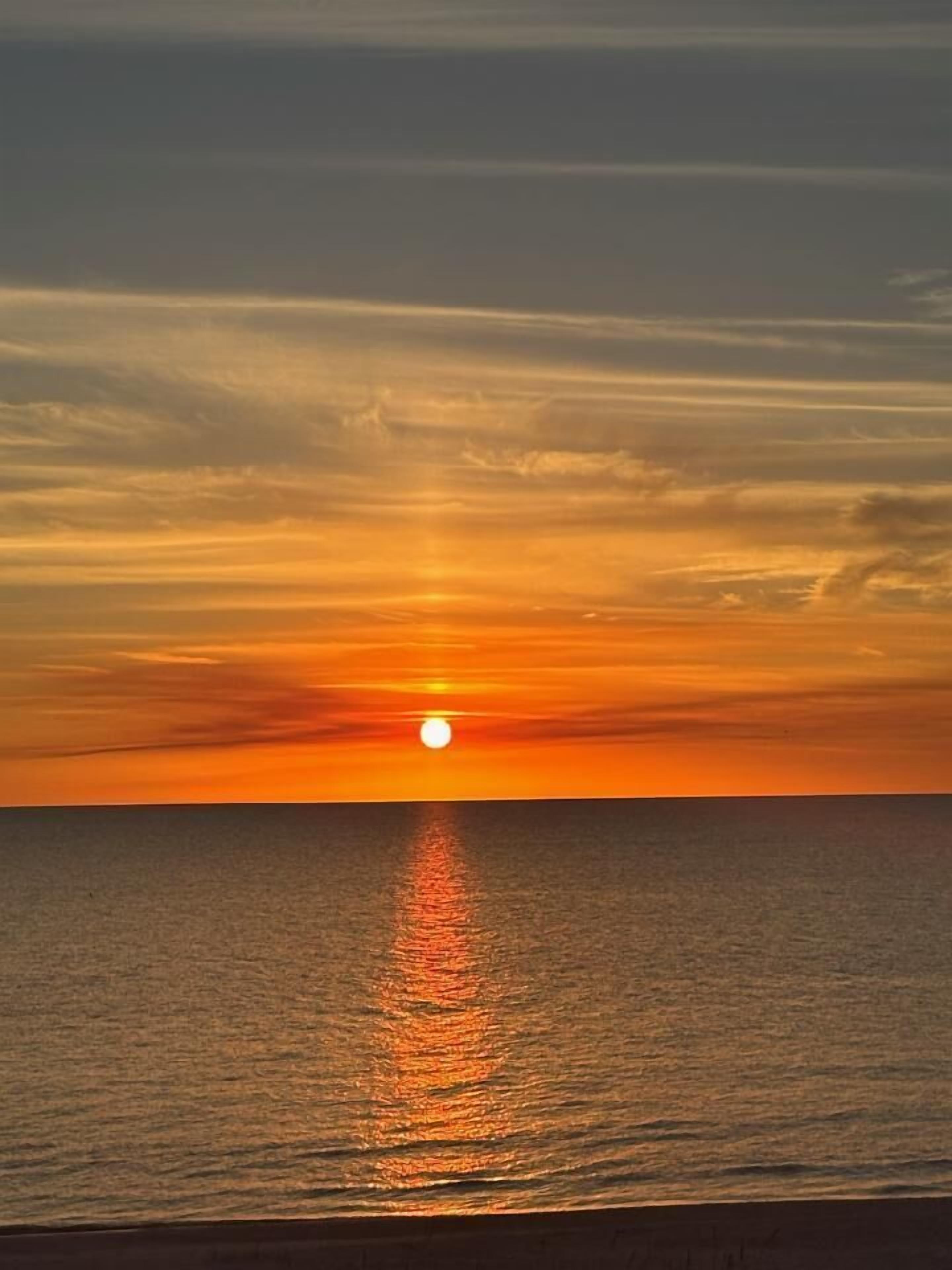 A sunset over a calm sea with a visible horizon line.
