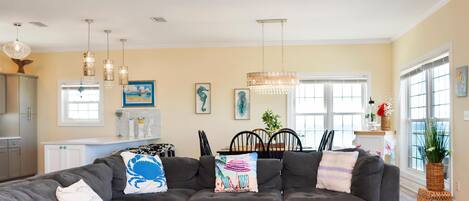 A living room with a sectional sofa, pendant lights, and a dining area with a table and chairs.