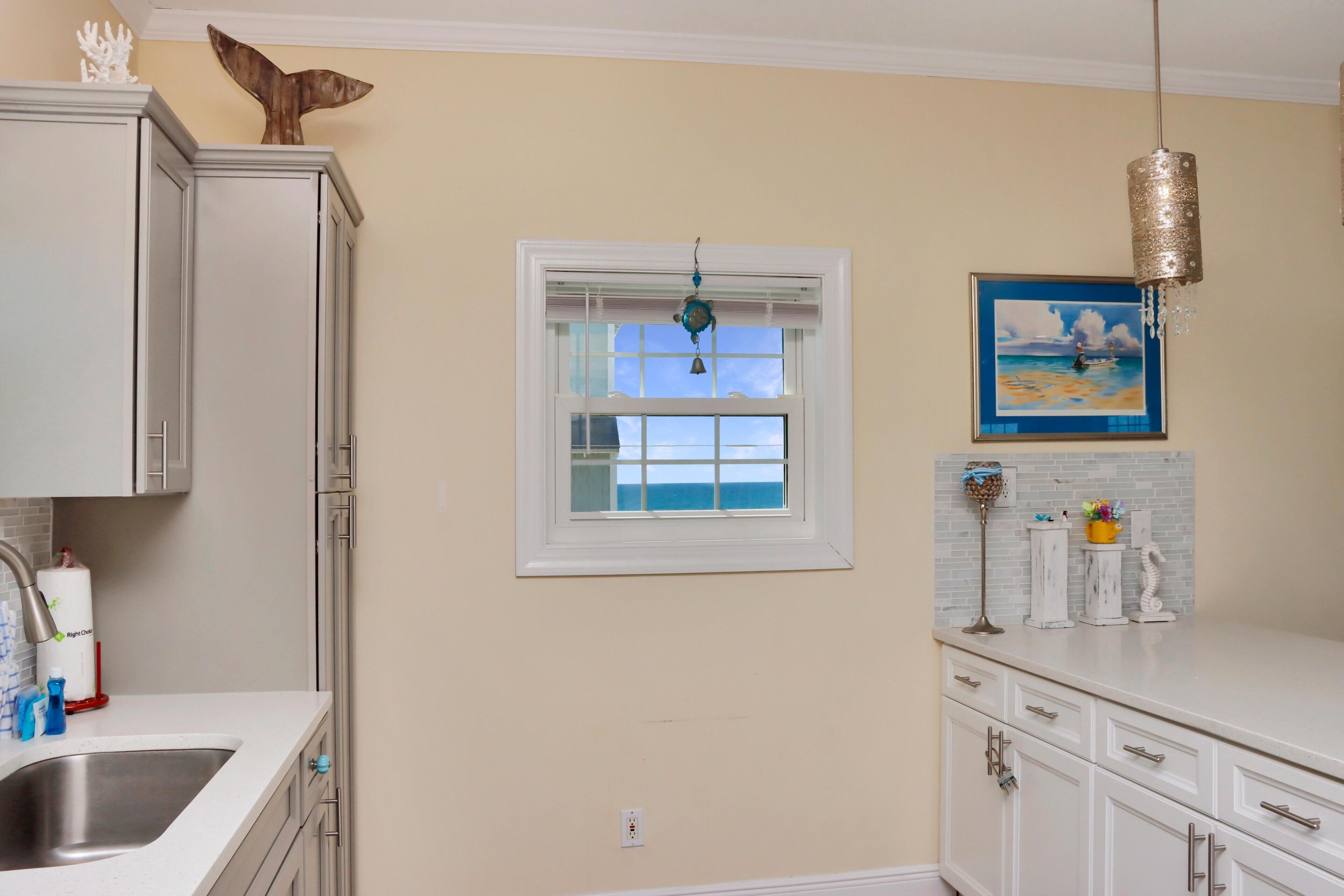 A kitchen with a window, white cabinets, a sink, and a decorative whale tail on the wall.