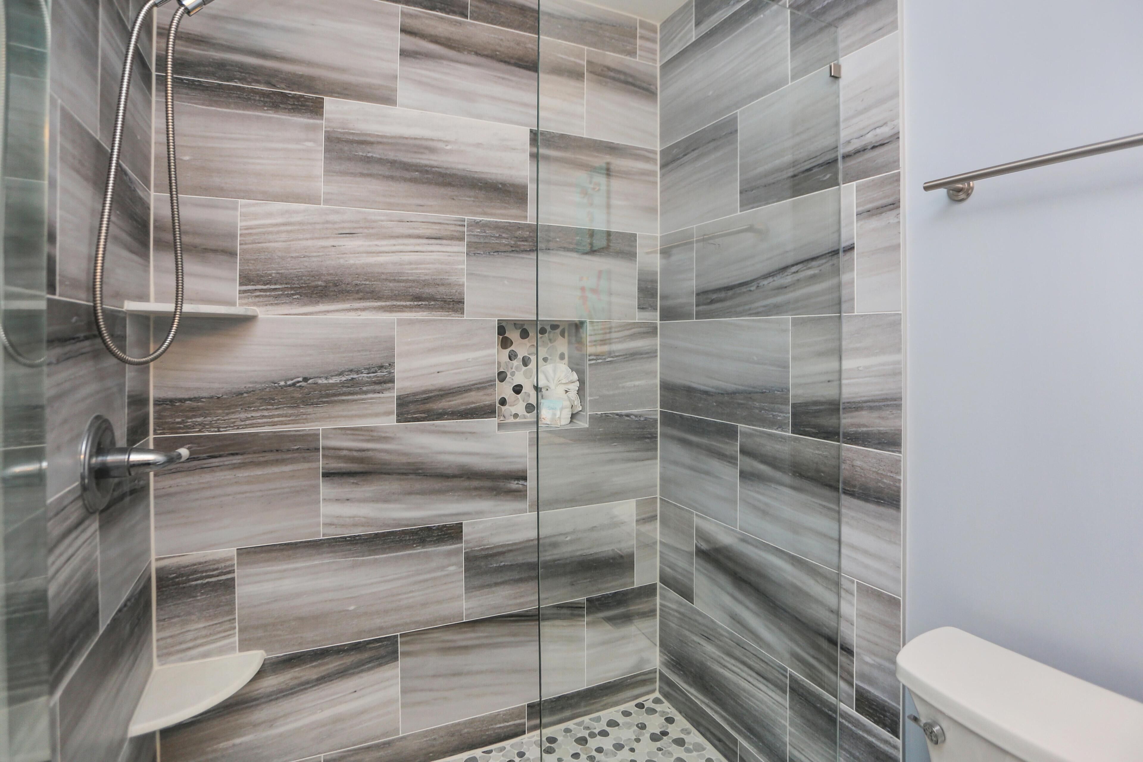 A bathroom with a shower, toilet, and a handrail.