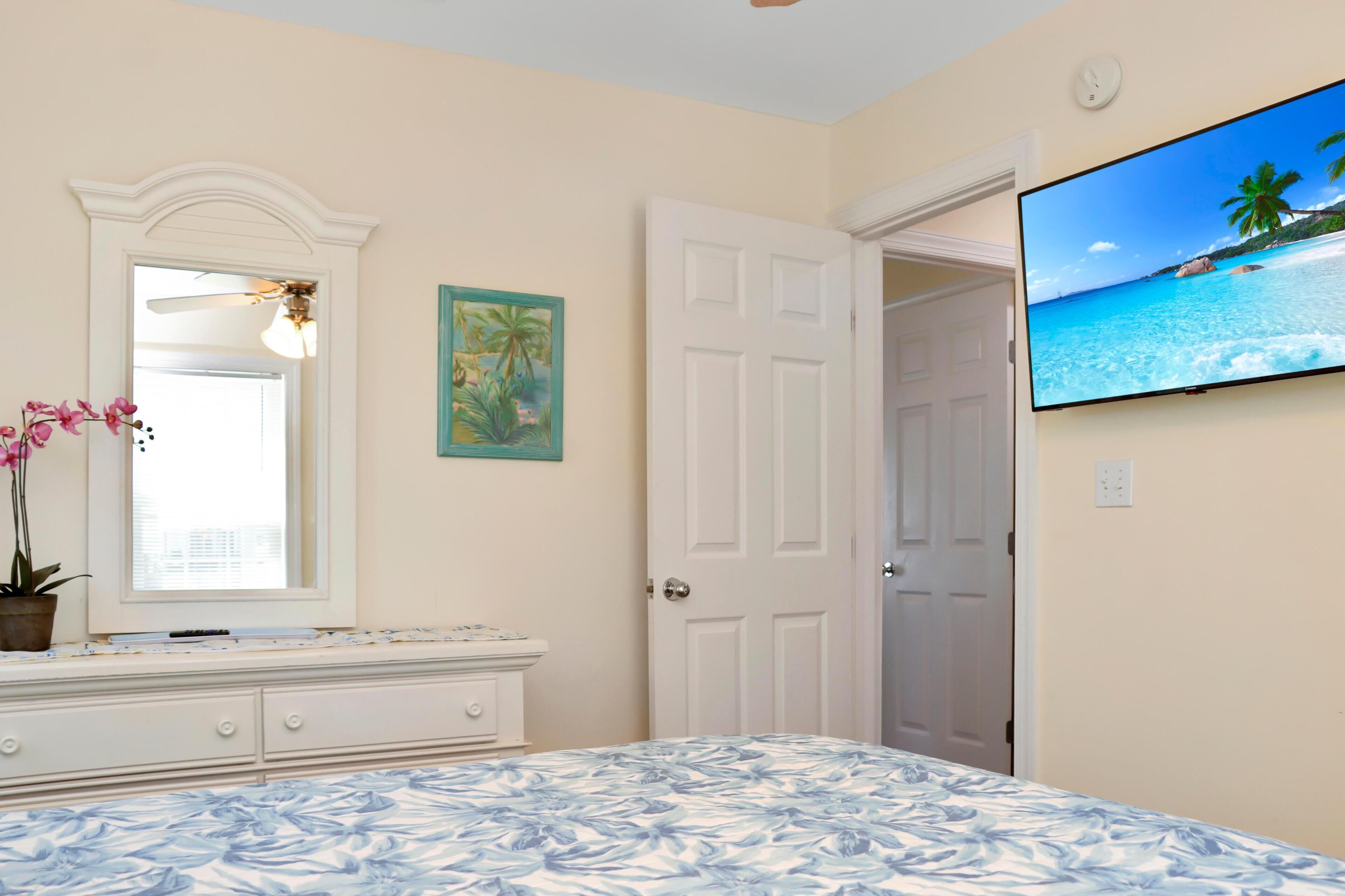 A bedroom with a bed, a dresser, a mirror, a television, and a door.