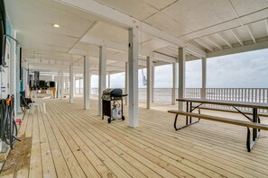 A covered wooden deck with a grill cart, benches, and a view of the sea.