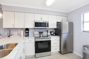 A modern kitchen with white cabinets, stainless steel appliances, a double sink, and a window with blinds. - The Hidden Pearl (Port St. Joe)