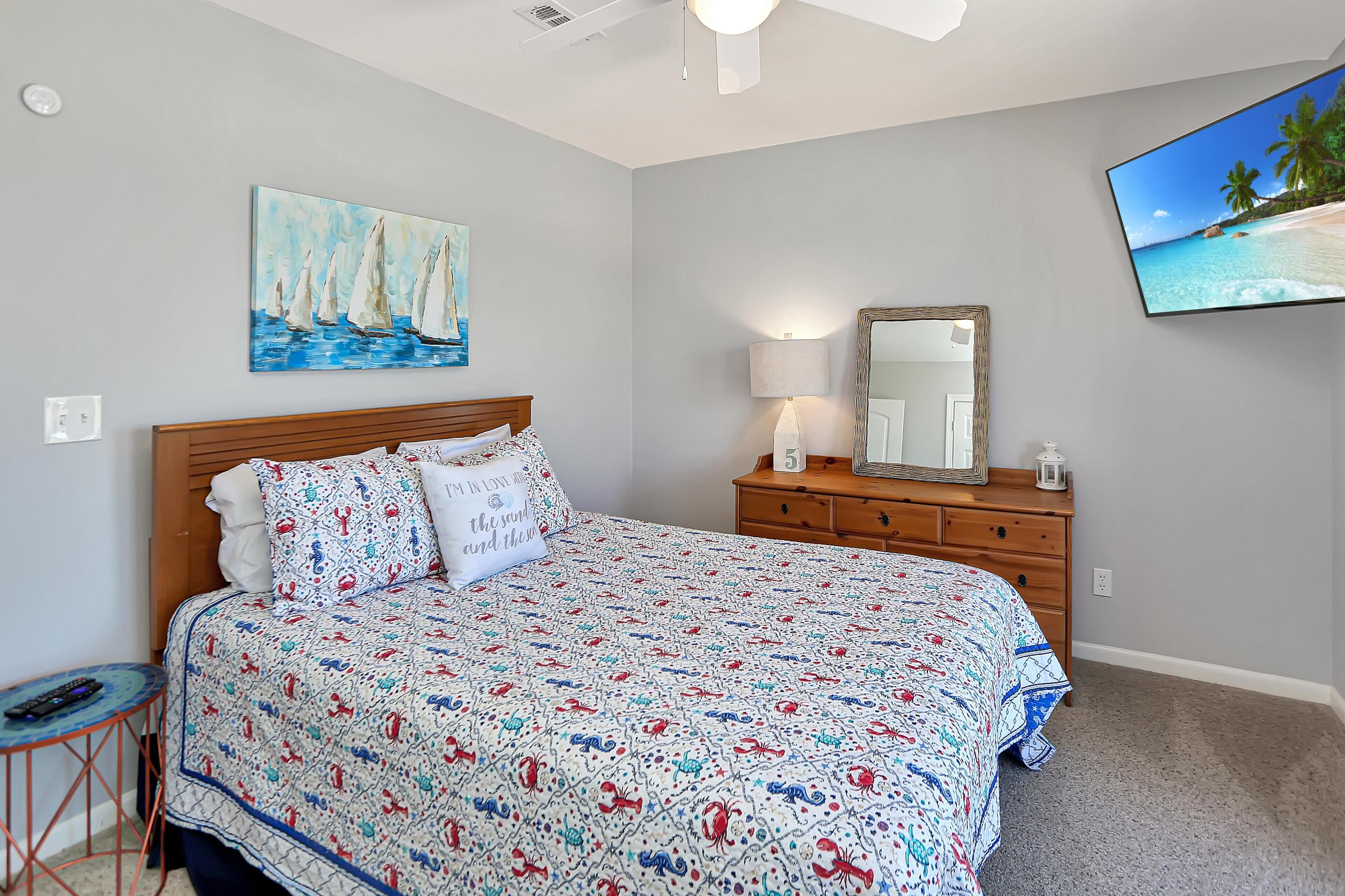 A bedroom with a bed, a nightstand, a lamp, a dresser, a painting, and a TV.