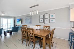 A dining area with a wooden table and chairs, a ceiling fan, and wall-mounted artwork. - The Hidden Pearl (Port St. Joe)