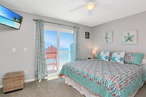 A bedroom with a bed, a television on the wall, and a balcony with a view of the ocean.