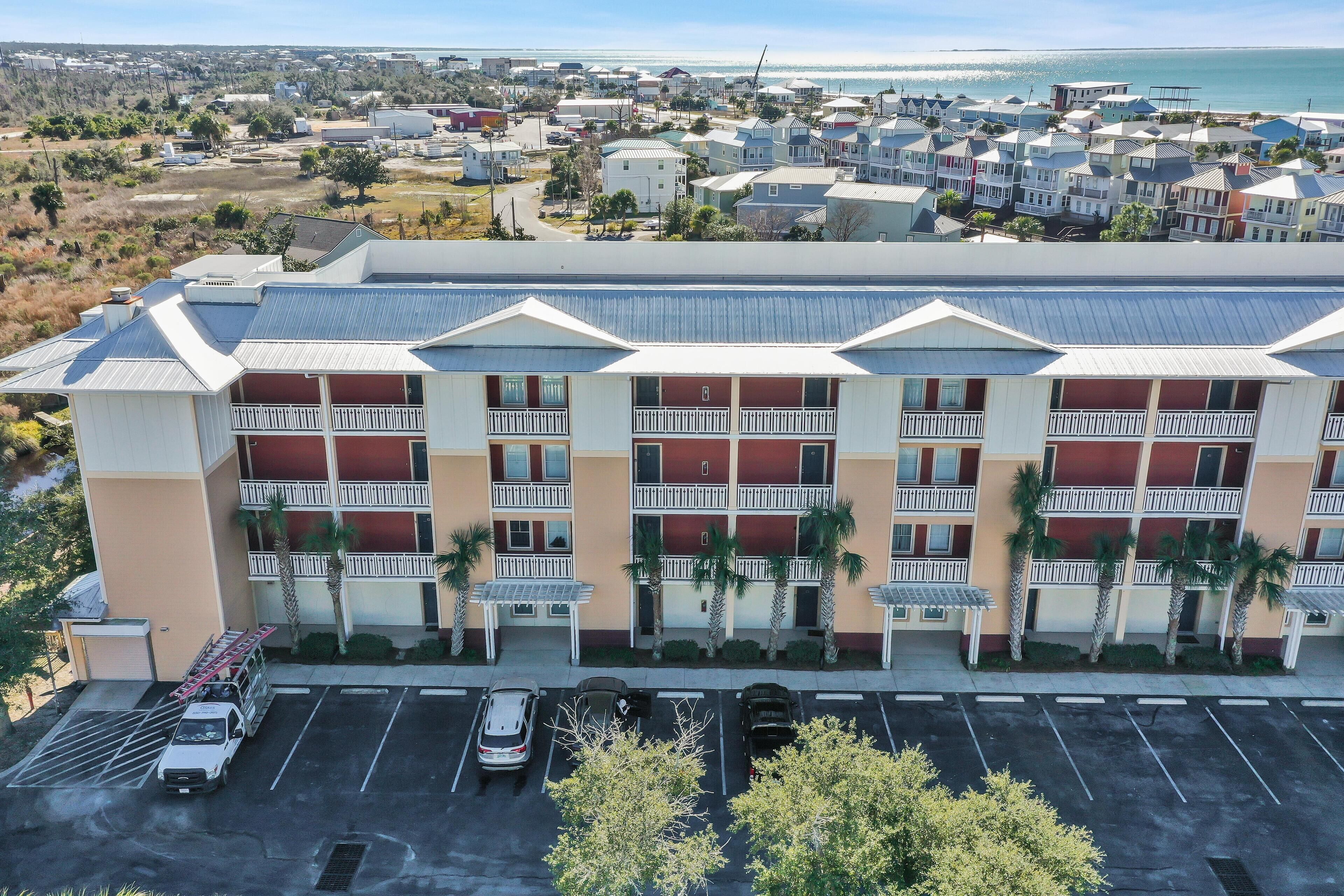 A multi-story hotel with a parking lot in front, featuring a row of balconies and palm trees.