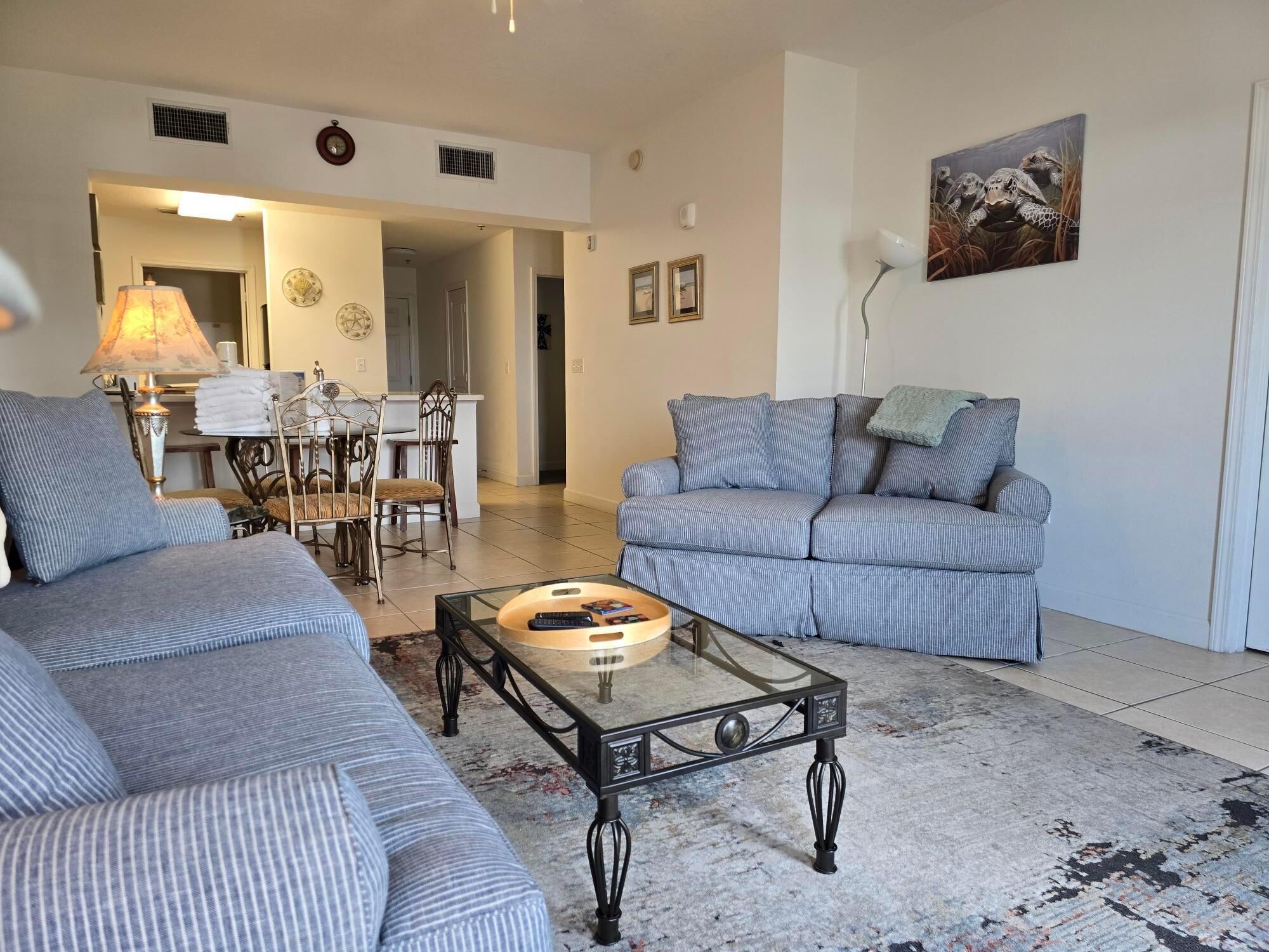 Ein Wohnzimmer mit gestreiften Sofas, einem Glastisch und einem Essbereich mit einer Chandelier.