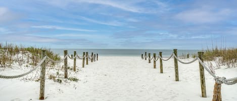 A sandy beach with wooden posts and ropes, leading to the ocean.