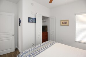 A bedroom with a bed, a wardrobe, a dresser, a framed picture, and a window with blinds. - Waterside Village Condo 302 (Port St. Joe)