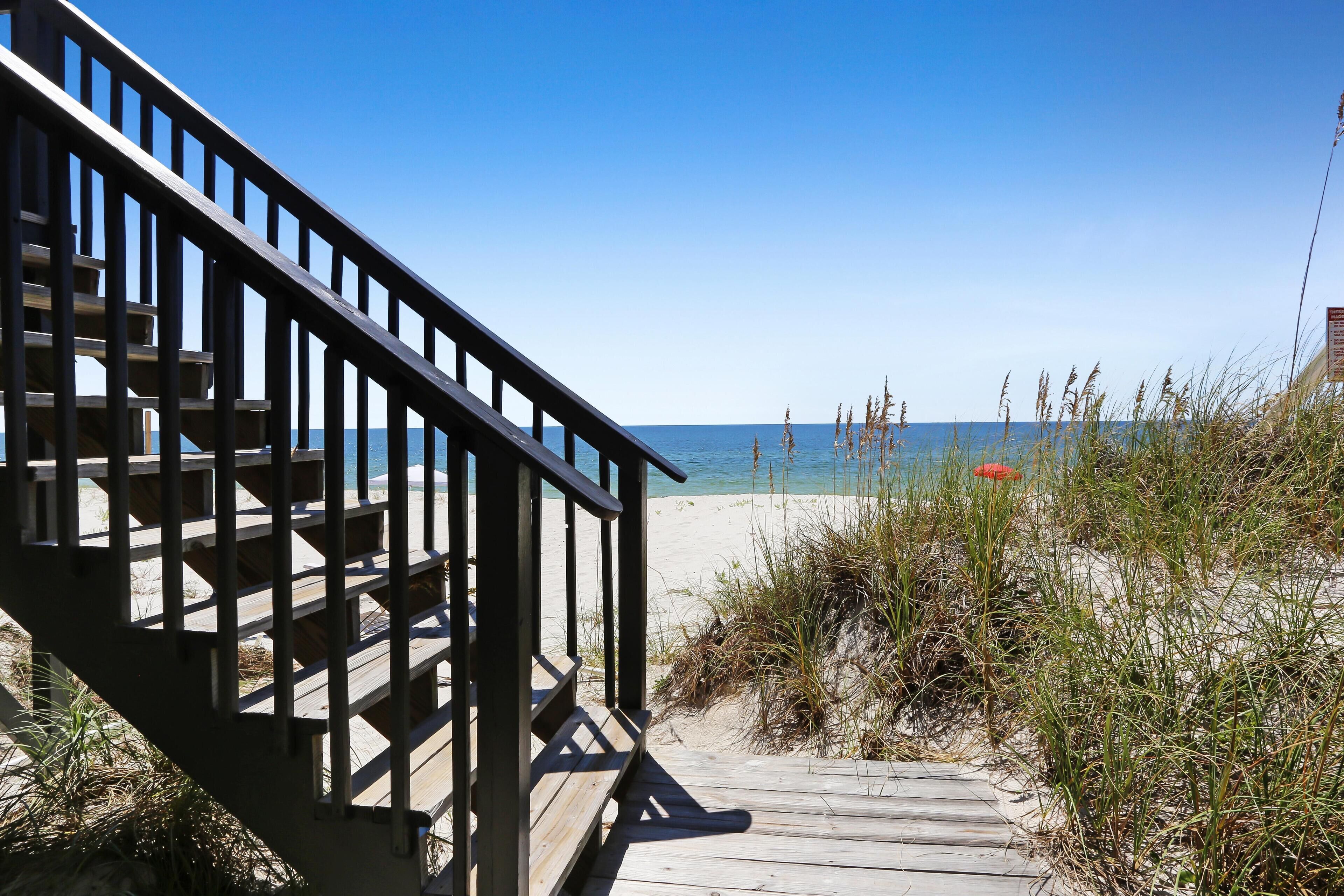 A wooden boardwalk leading to a beach with a clear view of the ocean.