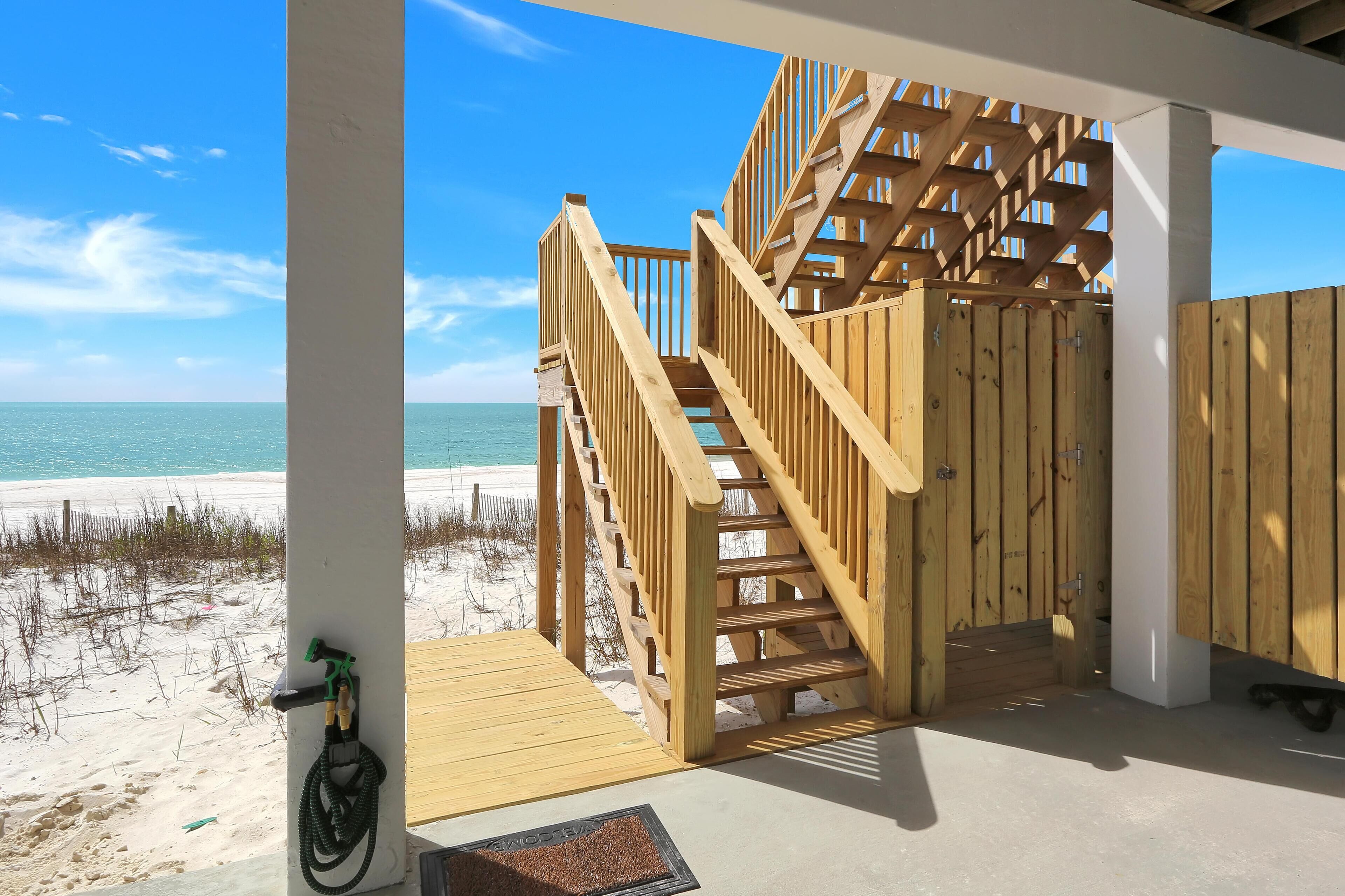 Un escalier en bois mène à une zone de plage d’où l’on a une vue sur l’océan.