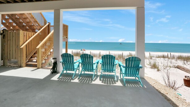 A covered outdoor area with a wooden staircase leading to a beach view. There are four green Adirondack chairs arranged in a row. - Beach Fantasies B (Port St. Joe)
