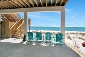 A covered outdoor area with a wooden staircase leading to a beach view. There are four green Adirondack chairs arranged in a row. - Beach Fantasies B (Port St. Joe)