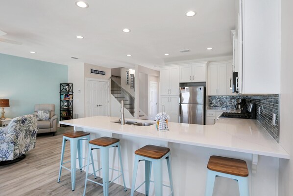 A modern kitchen with white cabinets, a large island with stools, stainless steel appliances, and a staircase leading to another level.